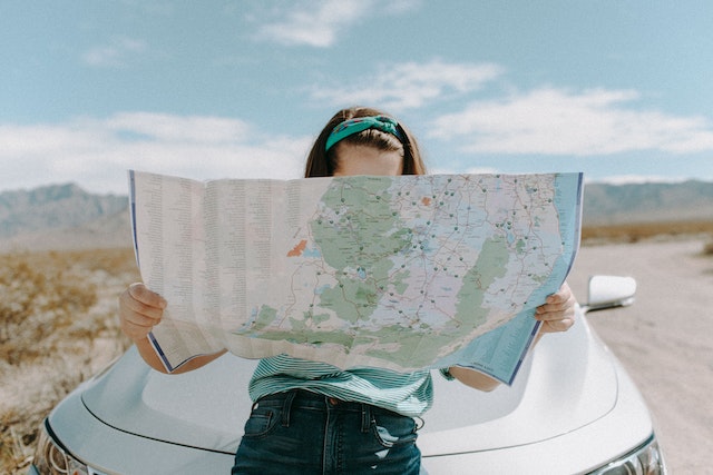 A woman reading a physical map in front of her car.