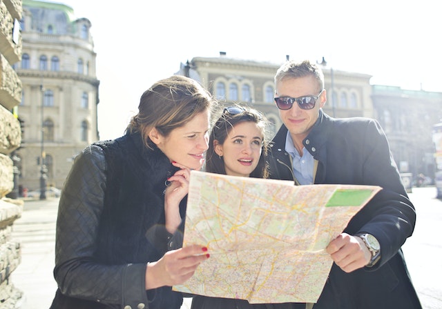 Two ladies and a man checking a physical map for the coordinates of a certain place in the city.