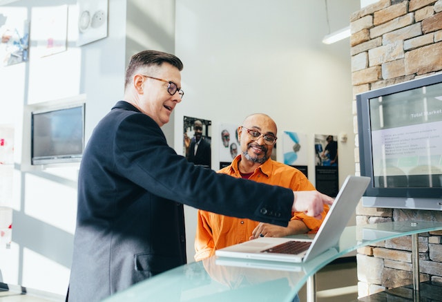 Man pointing to laptop computer in conversations with a coworker.