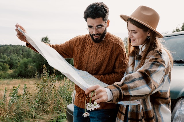 A couple in front of their car reading a physical reference map.