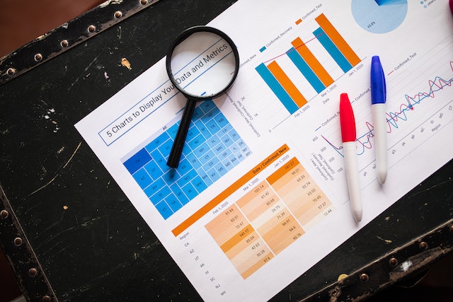 Magnifying glass and markers on paper with various Excel charts, graphs and data using conditional formatting.