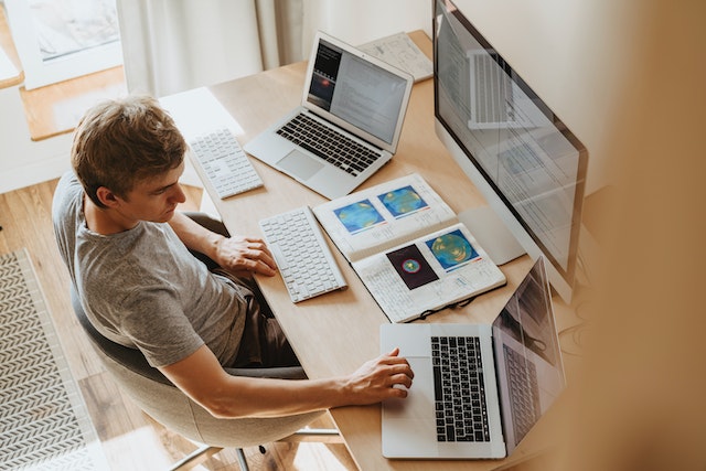Man using three computers while referencing a geographic heat map.