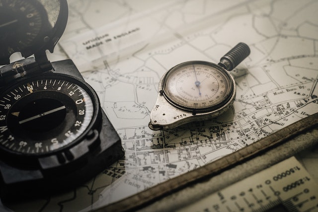 A black and silver compasses on top of a physical map.